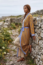 Kimono largo Shimauma, corazones azules, amarillo: modelo apoyada en la pared, en un sendero costero de Galicia
