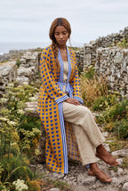 Kimono largo Shimauma, corazones azules, amarillo: modelo sentada de lado con las piernas cruzadas, en un sendero costero de Galicia