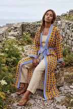 Kimono largo Shimauma, corazones azules, amarillo: modelo sentada con una pierna estirada, en un sendero costero de Galicia