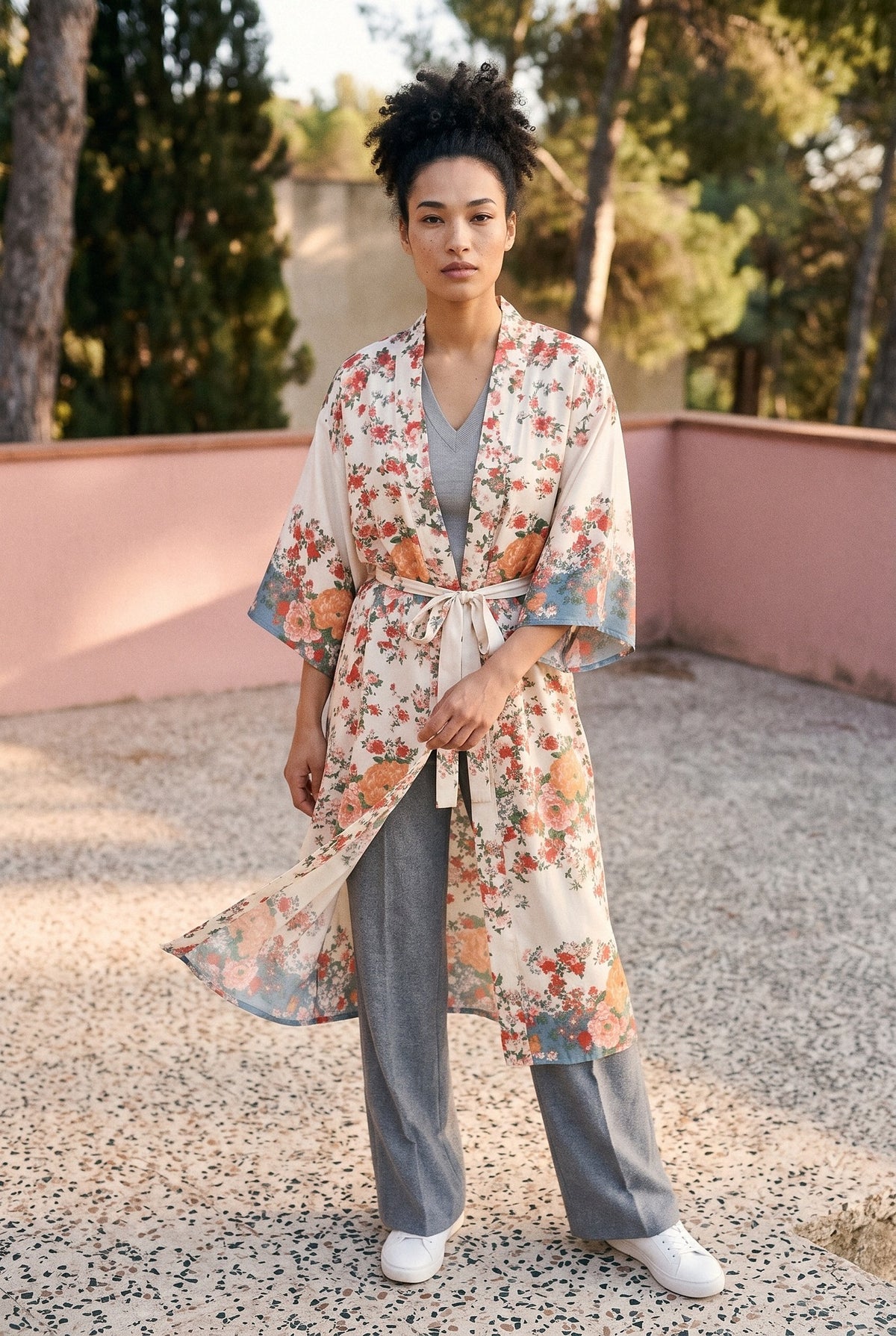 Kimono largo Shiro, flores sobre crudo: modelo con el tejido movido por la brisa, en la terraza de una villa de los años 50 con muro rosa
