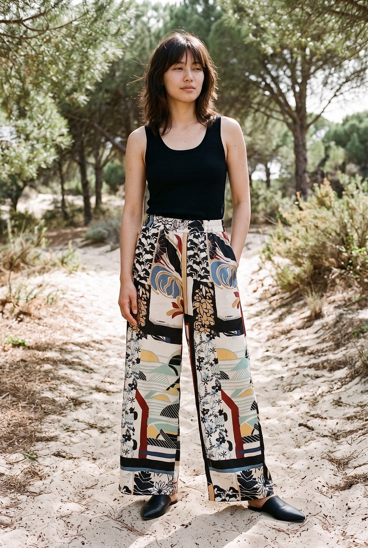 Pantalón kimono Kintsugi, palazzo estampado, negro y crudo: modelo con la mano en la cintura, en un sendero de dunas con pinos de Huelva