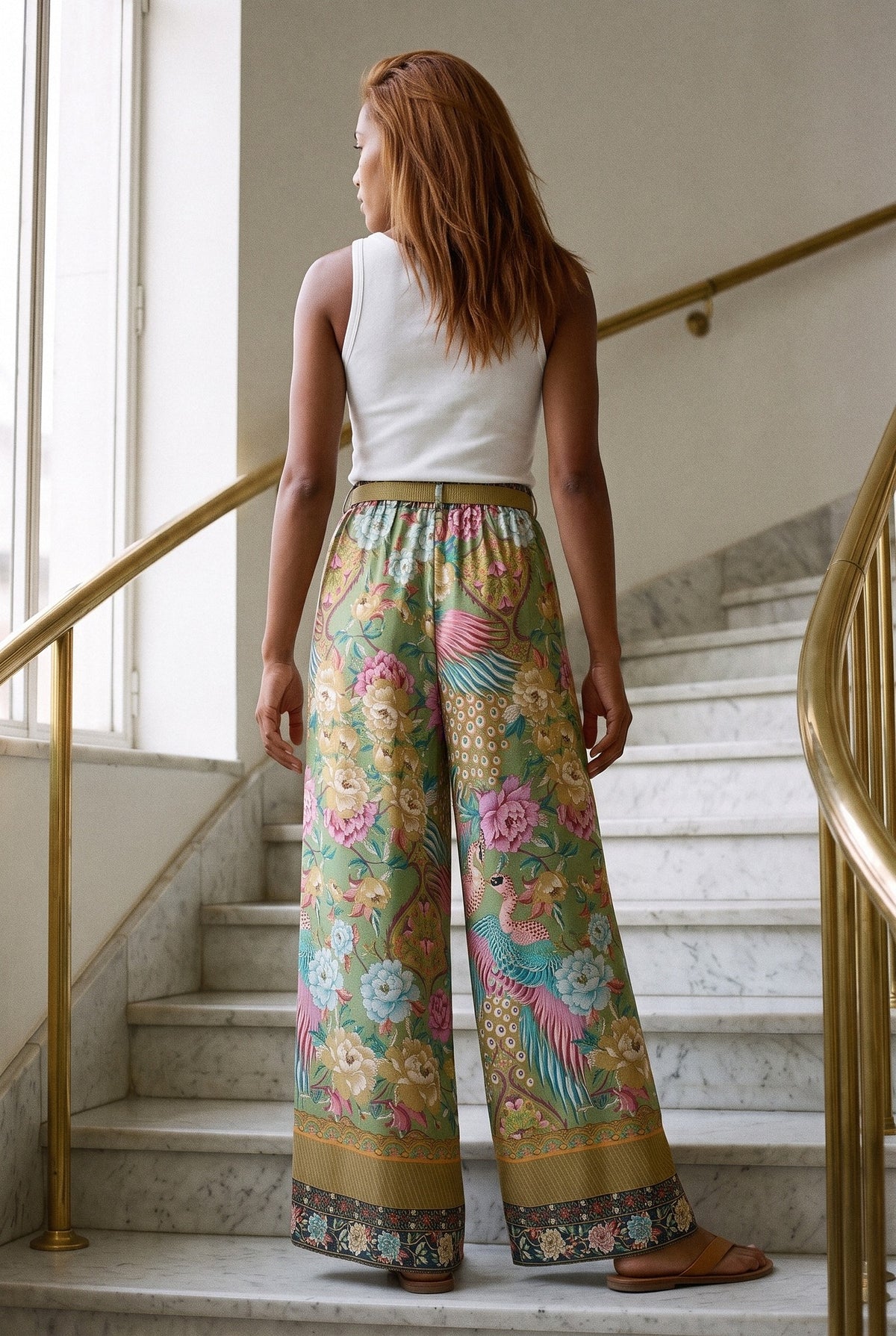 Pantalón kimono Kujaku, palazzo pavo real, verde: vista de espaldas, en una escalera de mármol con pasamanos de latón