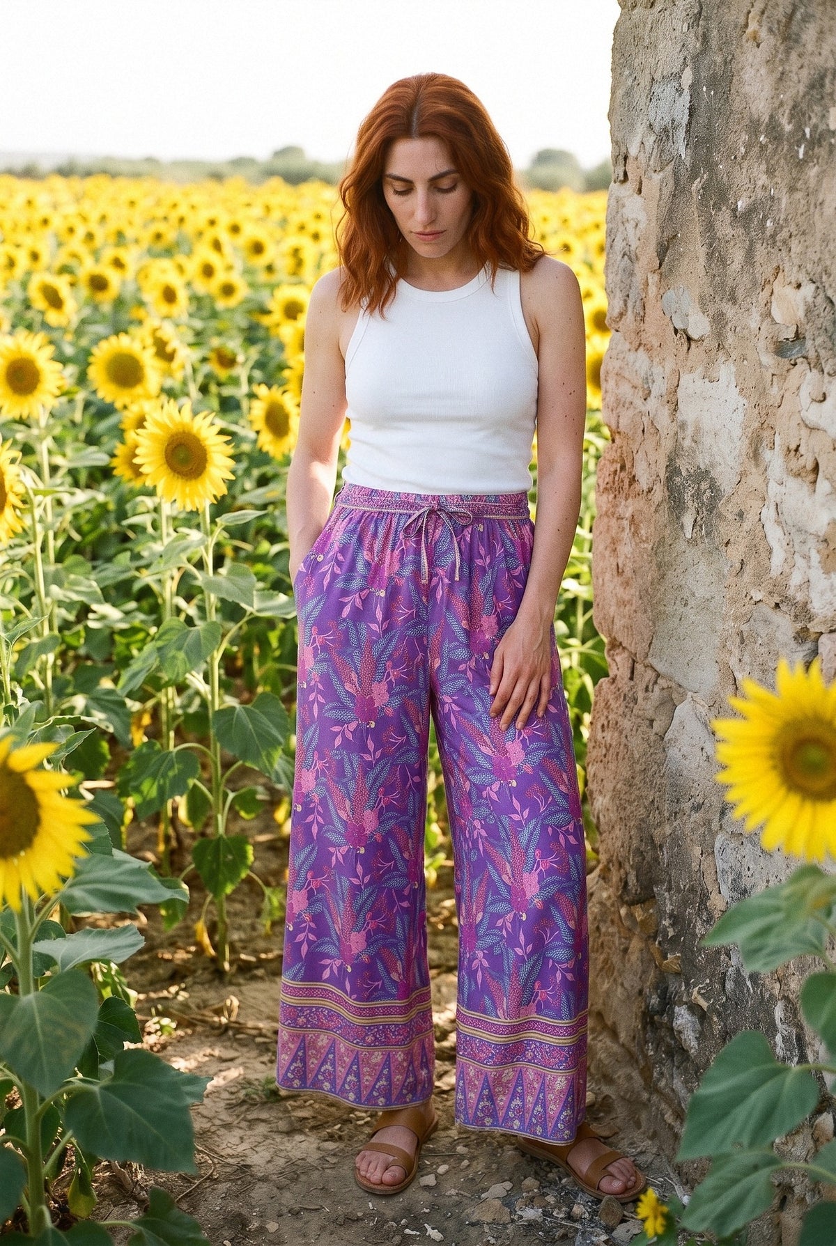 Pantalón kimono Murasaki, palazzo floral, morado: modelo con la mano en la cintura, en un campo de girasoles de Córdoba