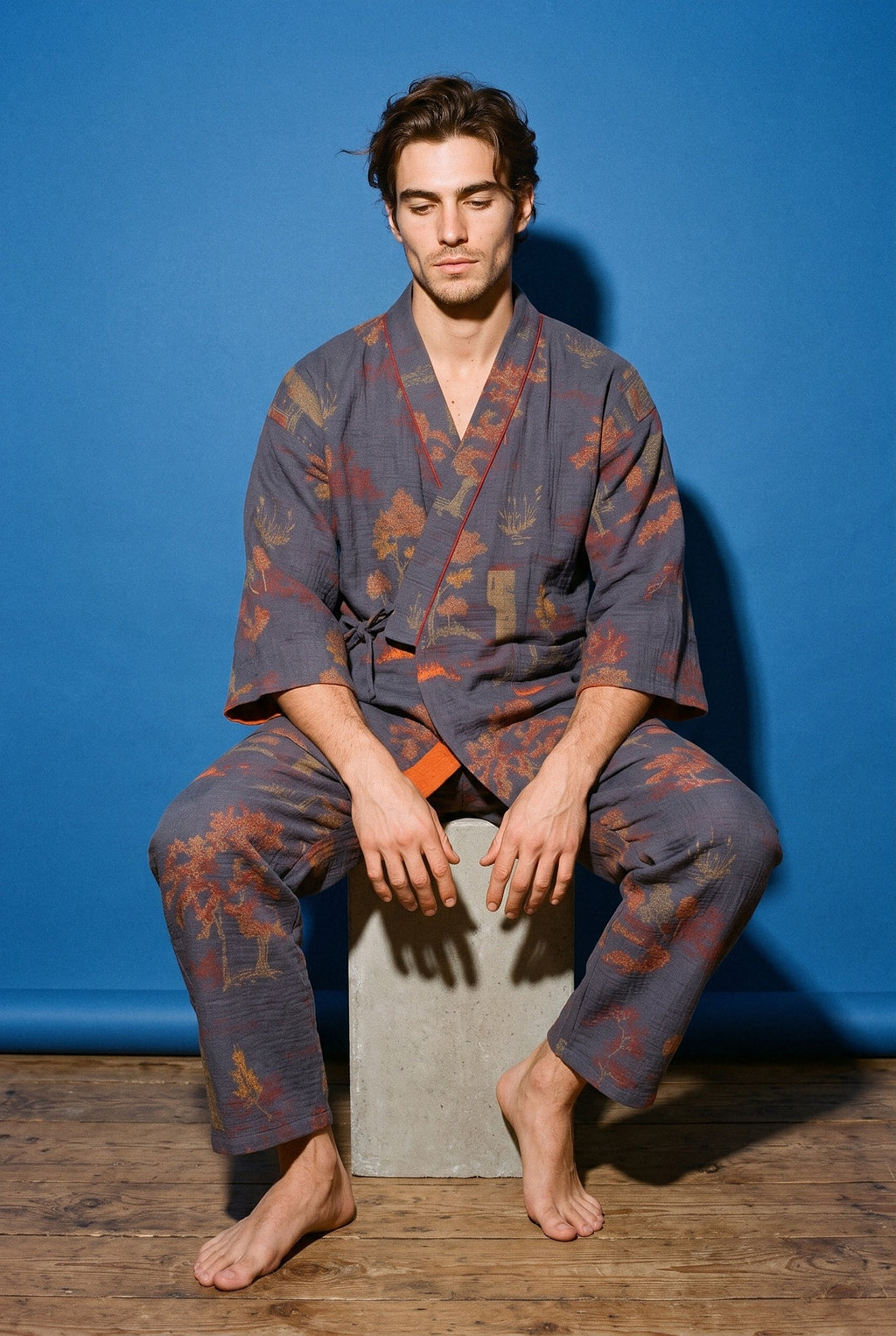 Pijama kimono Momiji, chaqueta y pantalón, azul marino: modelo sentado en un bloque, en estudio, fondo azul cobalto