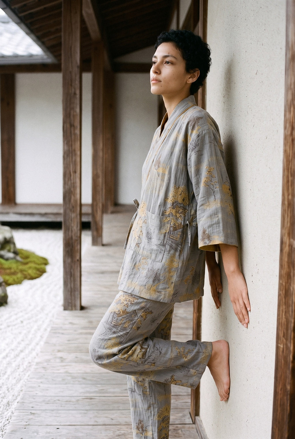 Pijama kimono Momiji, chaqueta y pantalón, gris: modelo apoyada en la pared, en un jardín de grava blanca rastrillada