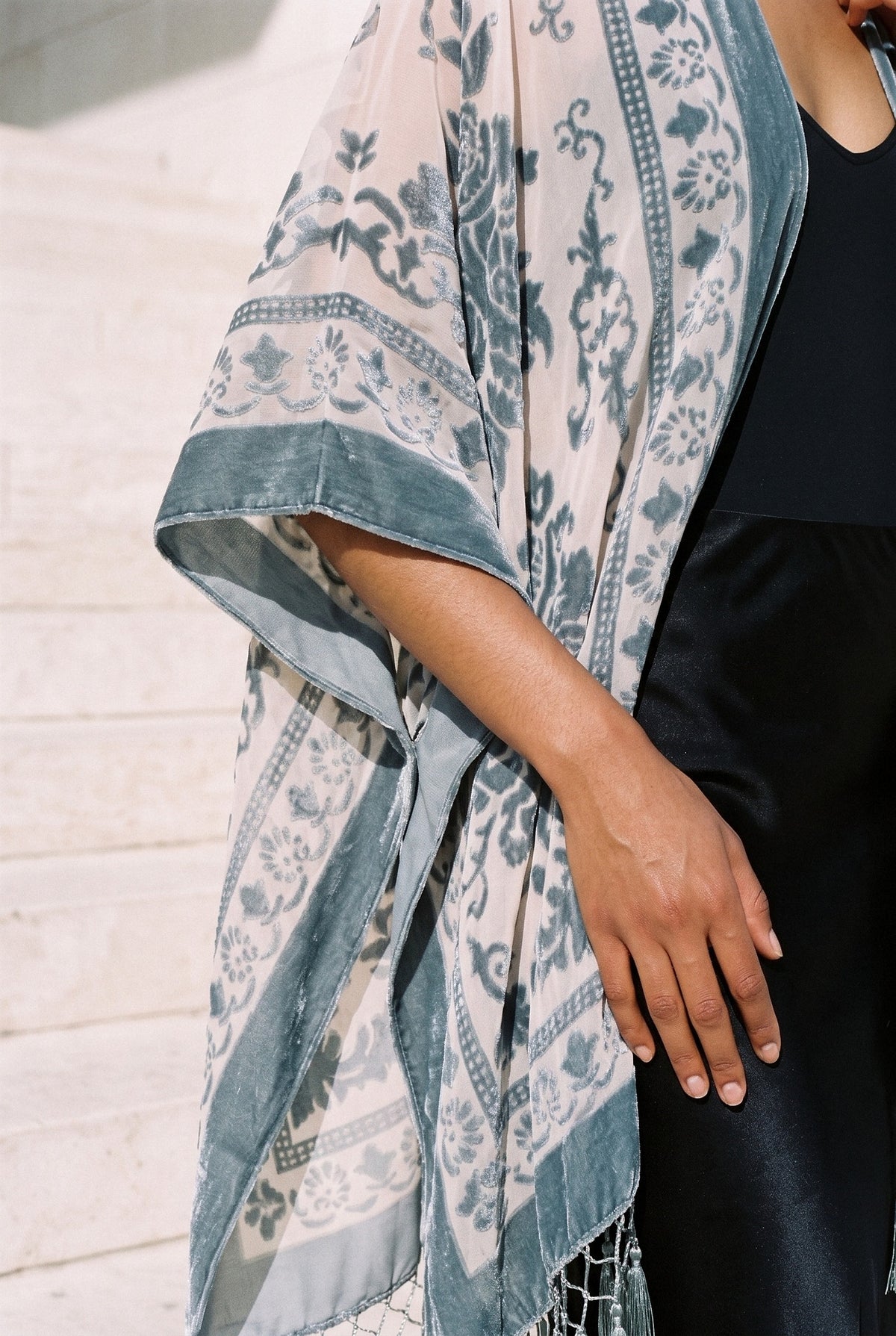 Poncho kimono Kage, terciopelo devoré, gris azulado: detalle de la manga y del estampado, en las escaleras de piedra clara de un museo