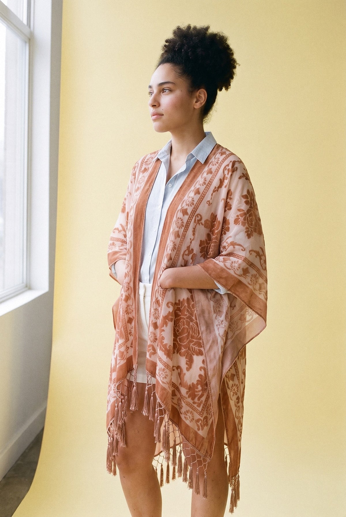 Poncho kimono Kage, terciopelo devoré, melocotón: modelo con las manos dentro de las mangas, en estudio, fondo amarillo mantequilla