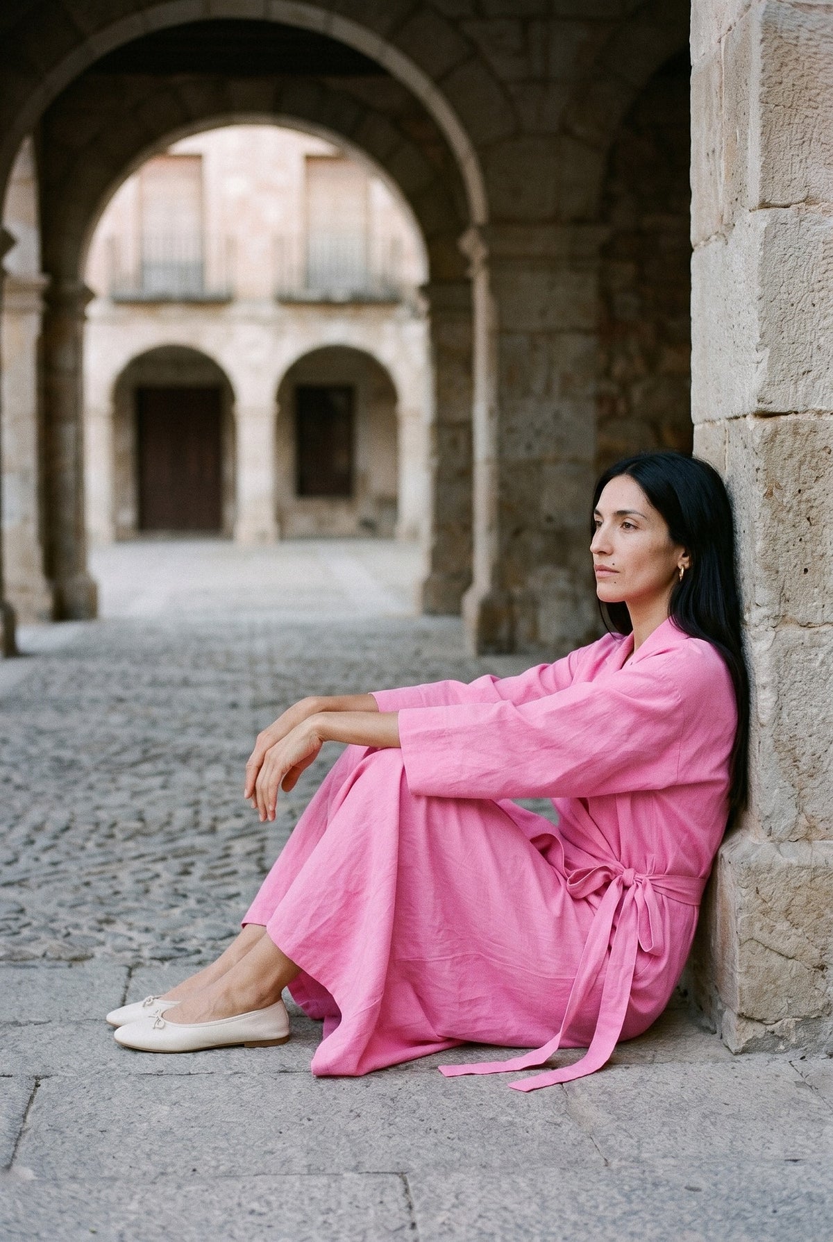 Vestido kimono Bara, algodón, rosa: modelo sentada contra la pared, bajo los soportales de una plaza mayor castellana