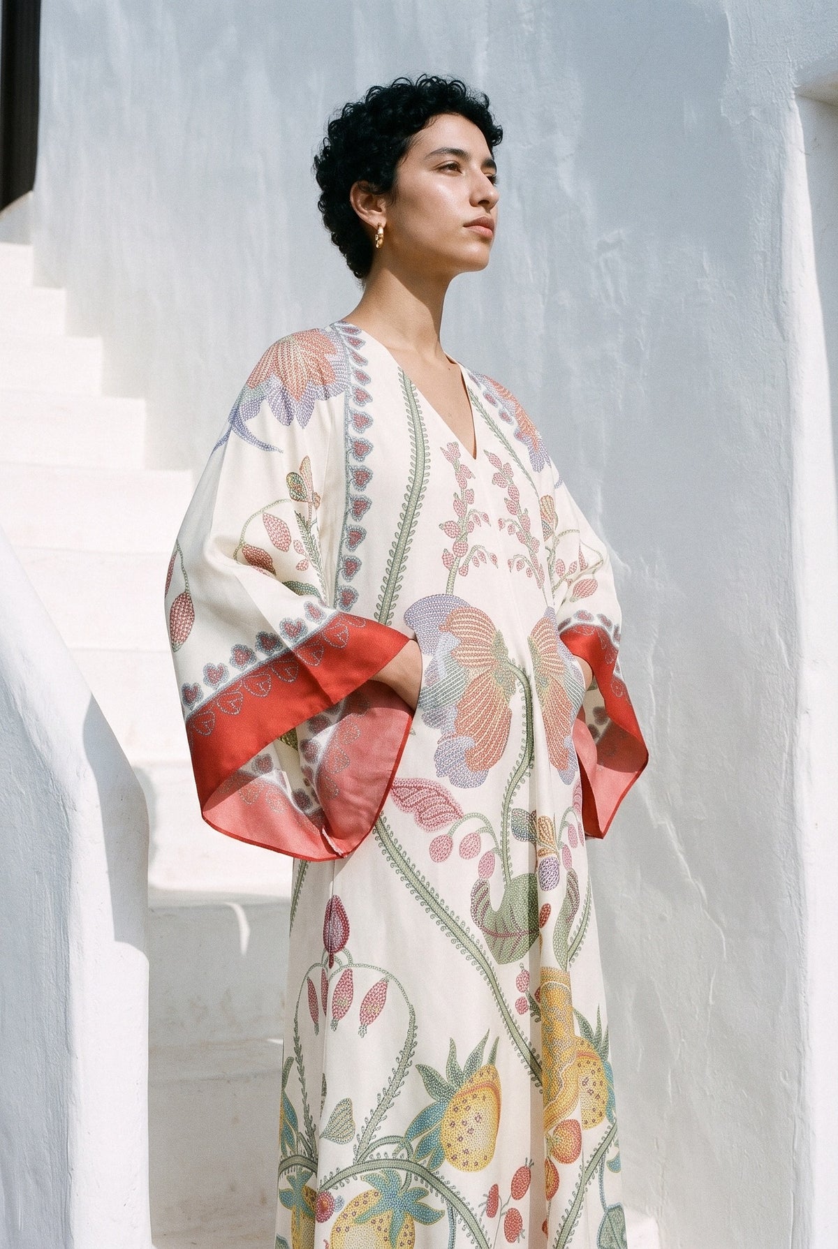 Vestido kimono Kōhaku, estampado blanco y rojo: modelo con las manos dentro de las mangas, en una escalera encalada de estilo ibicenco